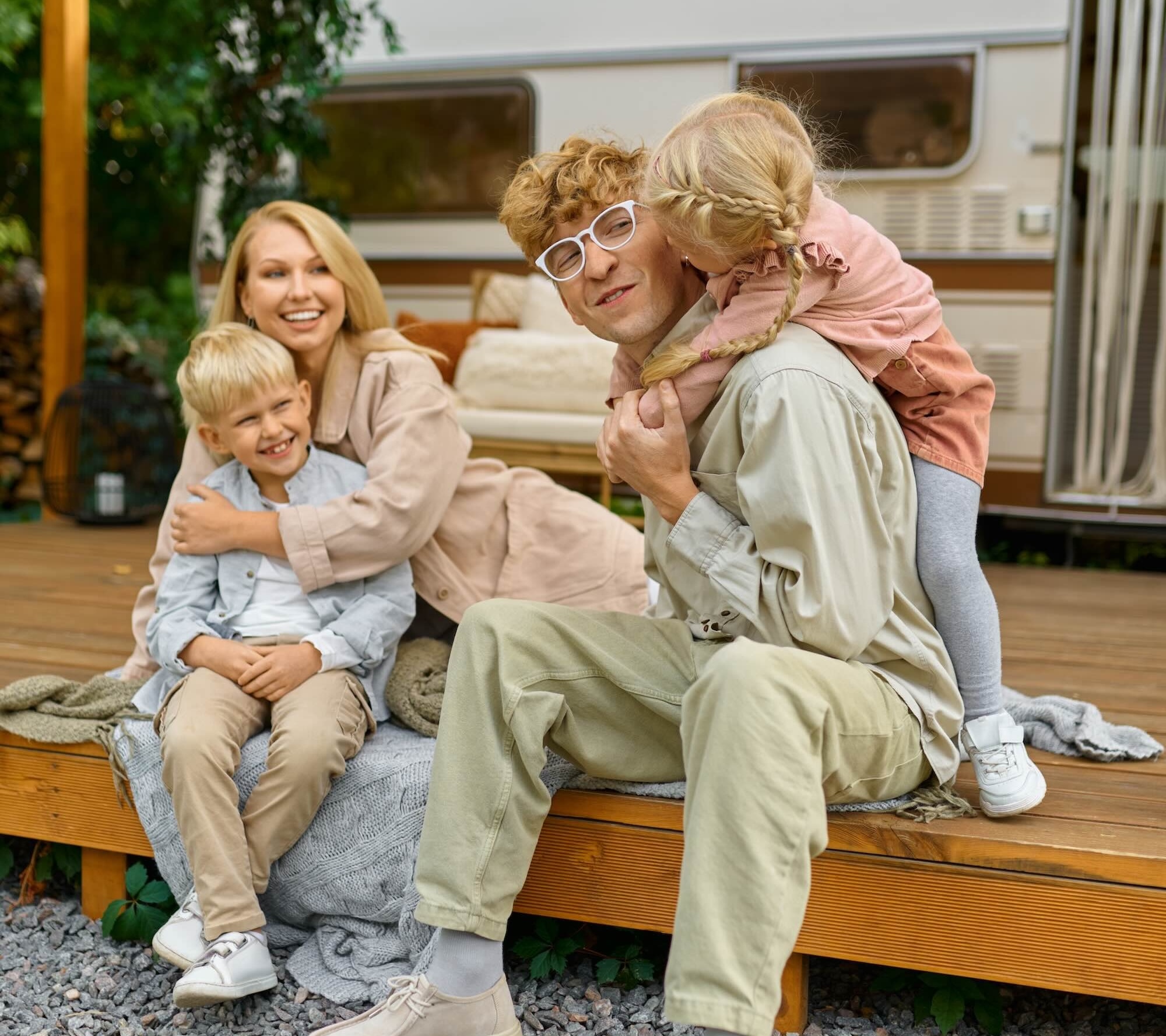 Happy family poses at the trailer, summer camping. Parents with children travel in camp car, nature and forest on background. Campsite adventure, travelling lifestyle